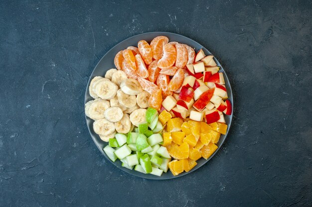 Draufsicht köstlicher Obstsalat in Scheiben geschnittene Mandarinen Äpfel Bananen und Orangen auf dunklem Hintergrund