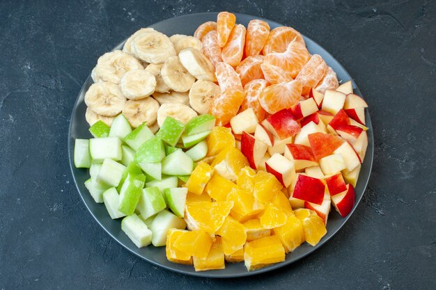 Draufsicht köstlicher Obstsalat in Scheiben geschnittene Mandarinen Äpfel Bananen und Orangen auf dunklem Hintergrund