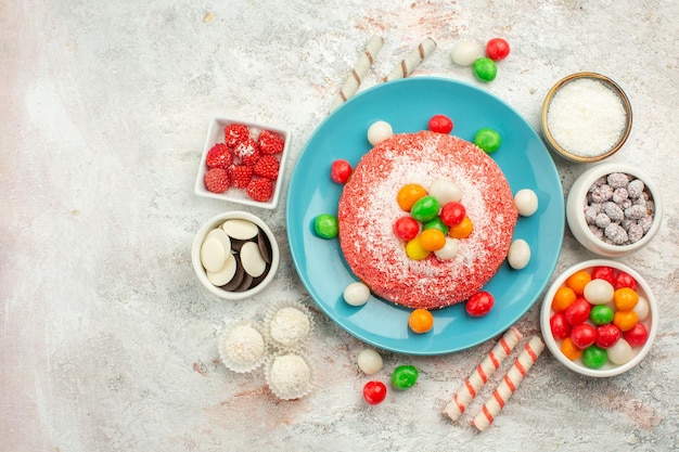 Draufsicht köstlicher rosa Kuchen mit bunten Bonbons auf der weißen Oberfläche Regenbogenfarbendessertkuchensüßigkeit