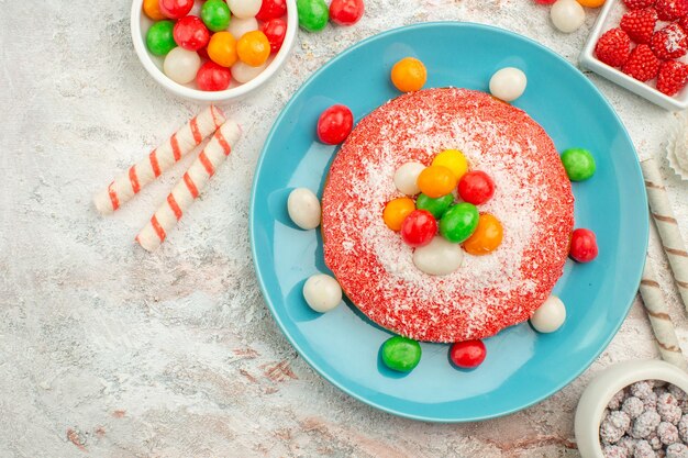 Draufsicht köstlicher rosa Kuchen mit bunten Süßigkeiten auf weißem Boden Süßigkeiten Dessert Farbe Regenbogen Goodie Cake