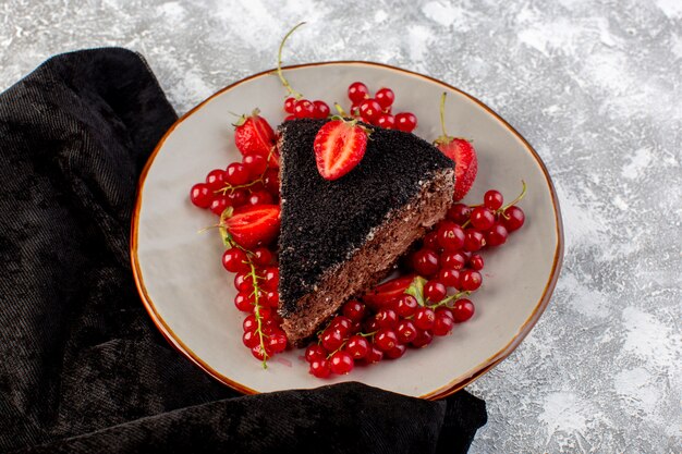 Draufsicht köstlicher Schokoladenkuchen geschnitten mit Schoko-Sahne und frischen roten Preiselbeeren auf dem grauen Schreibtischkuchen-Keksteigauflauf