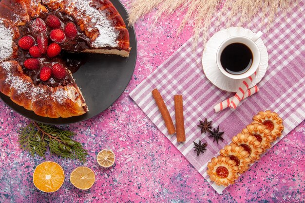 Draufsicht köstlicher Schokoladenkuchen mit Keksen und Tasse Tee auf hellrosa Schreibtischkeks süßer Zuckerdessertkuchen backen Kuchen