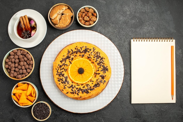 Draufsicht köstlicher süßer Kuchen mit Orangenscheiben und Tasse Tee auf dunkelgrauer Oberfläche Cookie Pie Keks Kuchen Dessert Tee