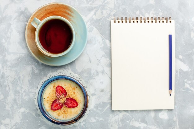 Draufsicht köstliches cremiges Dessert mit Notizblock mit frischen Erdbeeren und Tee auf hellweißem Hintergrunddesserteis süßer Fruchtgeschmack