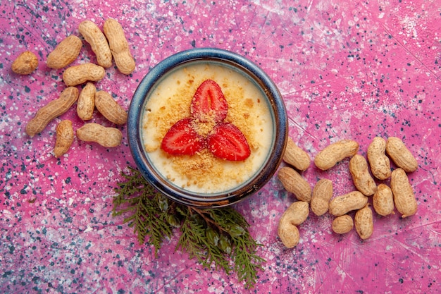 Draufsicht köstliches cremiges Dessert mit rot geschnittenen Erdbeeren und Erdnüssen auf der hellrosa Hintergrunddessert-Eiscremefarbe süße Fruchtbeere