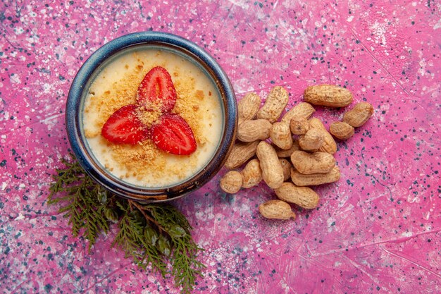 Draufsicht köstliches cremiges Dessert mit rot geschnittenen Erdbeeren und Erdnüssen auf der hellrosa Hintergrunddessert-Eiscremefarbe süße Fruchtbeere