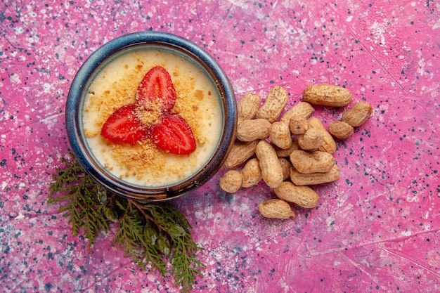 Draufsicht köstliches cremiges Dessert mit rot geschnittenen Erdbeeren und Erdnüssen auf der hellrosa Hintergrunddessert-Eiscremefarbe süße Fruchtbeere