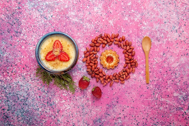 Draufsicht köstliches cremiges Dessert mit rot geschnittenen Erdbeeren und Erdnüssen auf der hellrosa Hintergrunddessert-Eiscremefarbe süße Fruchtbeere