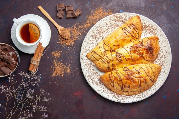 Draufsicht köstliches gebackenes Gebäck mit Tasse Tee auf dem dunklen Raum