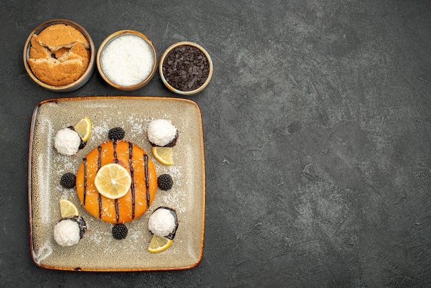 Draufsicht köstliches Kuchendessert mit Zitronenscheiben und Kokosbonbons auf dunklem Kuchendessert süßer Kuchensüßigkeitstee