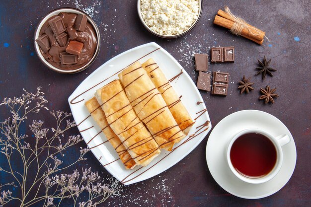 Draufsicht köstliches süßes Gebäck mit Schokolade und Tasse Tee auf dem dunklen Raum