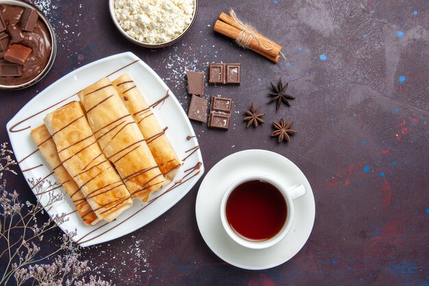 Draufsicht köstliches süßes Gebäck mit Schokolade und Tasse Tee auf dem dunklen Raum