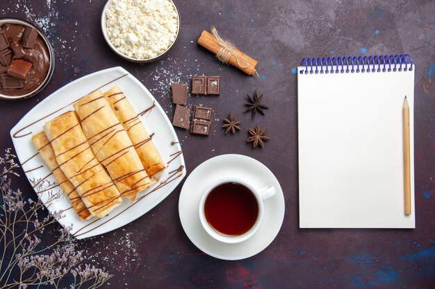 Draufsicht köstliches süßes Gebäck mit Schokolade und Tasse Tee auf dunklem Boden backen Dessertzuckerkekskuchen süß