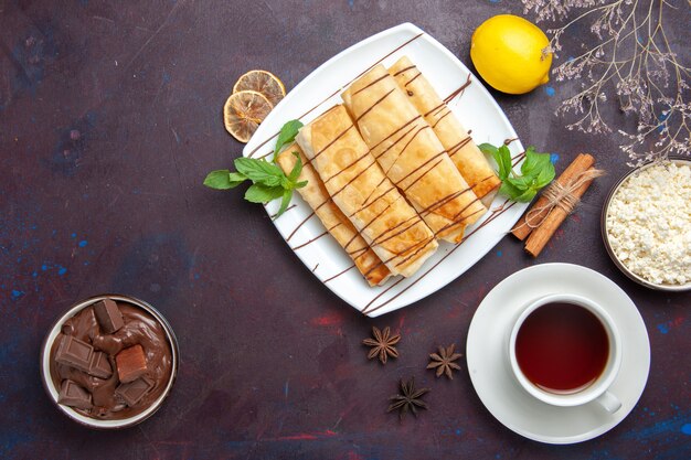 Draufsicht köstliches süßes Gebäck mit Tasse Tee und Schokolade auf dem dunklen Raum