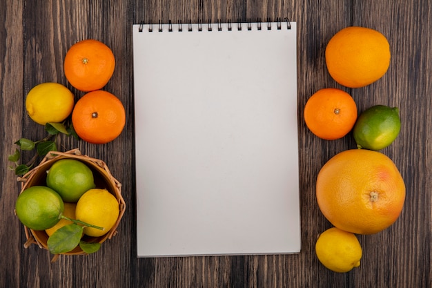 Draufsicht-Kopienraum-Notizblock mit Grapefruit-Orangen-Zitronen und Limetten in einem Korb auf einem hölzernen Hintergrund