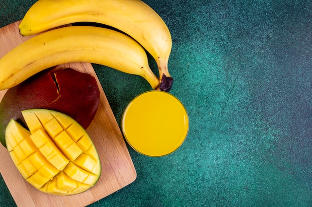 Draufsicht kopieren Raum geschnittene Mango mit Bananen an Bord mit Orangensaft auf Grün