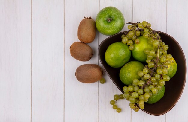 Draufsicht kopieren Raum Kiwi mit Apfel und Trauben mit Mandarinen in einer Schüssel auf weißer Wand