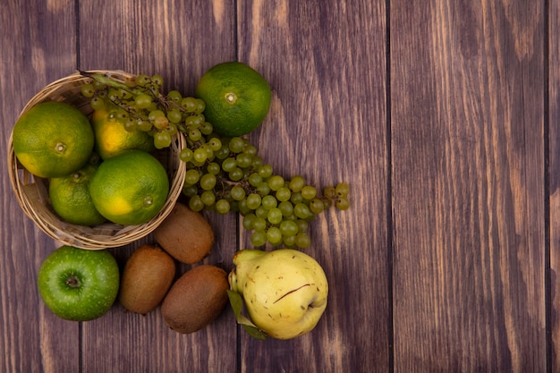 Draufsicht kopieren raumbirne mit kiwi-mandarinenäpfeln und -trauben in einem korb auf einer holzwand