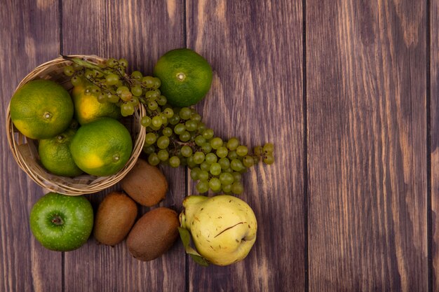 Draufsicht kopieren Raumbirne mit Kiwi-Mandarinenäpfeln und -trauben in einem Korb auf einer Holzwand