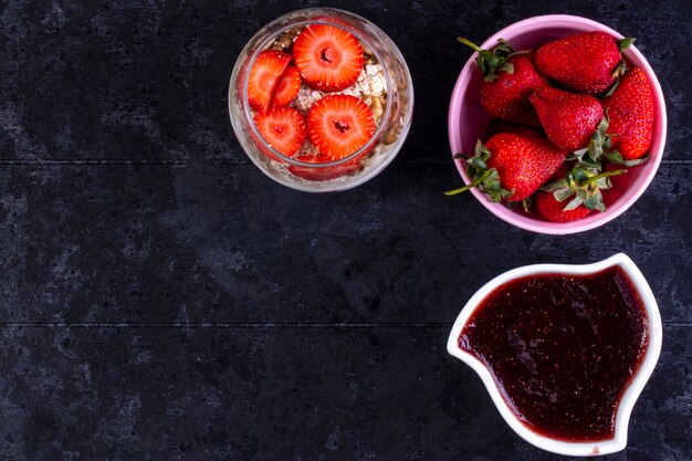 Draufsicht kopieren Raummüsli mit Früchten und Nüssen in einem Glas mit Erdbeeren in einer rosa Schüssel und Marmelade