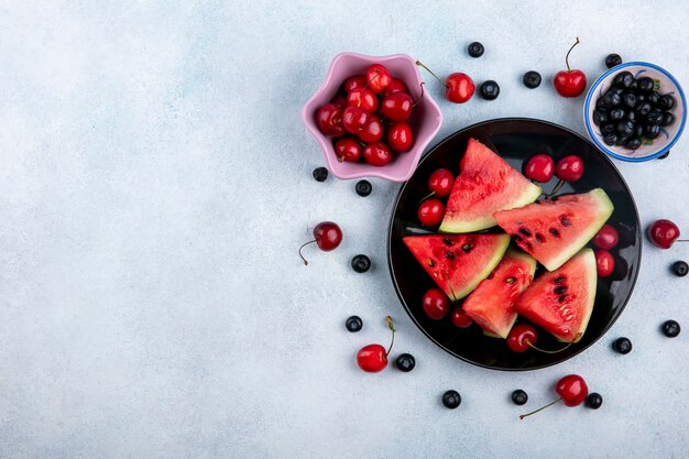 Draufsicht kopieren Raumscheiben der Wassermelone auf einem Teller mit Blaubeeren und Kirschen