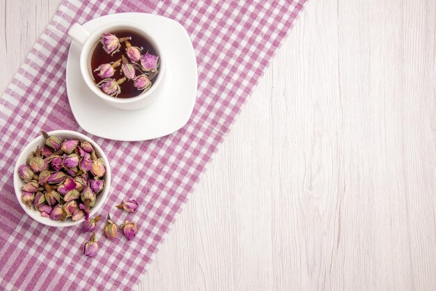 Draufsicht Kräutertee eine Tasse Kräutertee auf der Untertasse neben der Kräuterschale auf der karierten Tischdecke auf dem Tisch