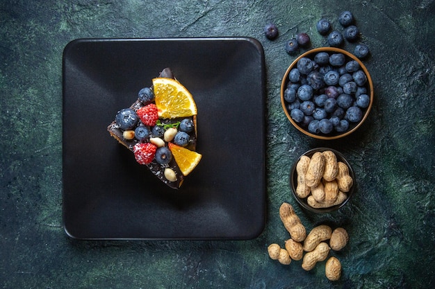 Draufsicht Kuchenscheibe köstlichen Schokoladenkuchen mit Früchten innerhalb Platte auf Dunkelheit