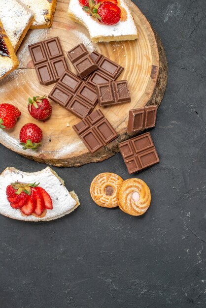 Draufsicht-Kuchenscheiben mit Schokoriegeln und Keksen auf grauem Schreibtisch