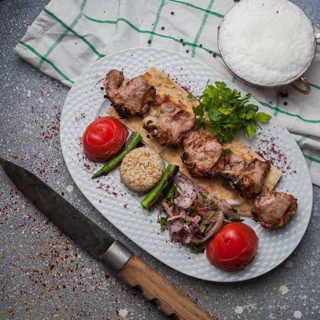 Draufsicht Lammkebab mit gebratenem Gemüse und gehackter Zwiebel und Ayran und Messer im weißen Teller