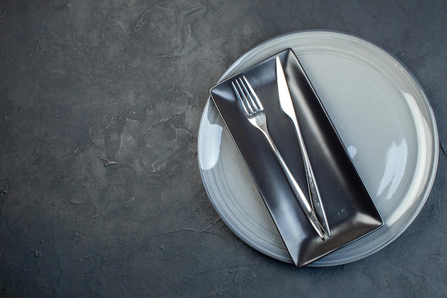 Draufsicht langer schwarzer Teller mit Gabel und Messer in grauer Platte auf dunklem Hintergrund Glasbesteck bunte Weiblichkeit horizontales Küchenessen