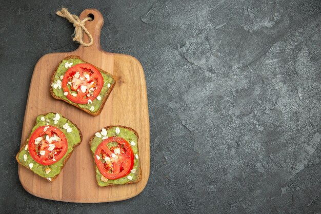 Draufsicht leckere Avocado-Sandwiches mit geschnittenen roten Tomaten auf dem grauen Hintergrund Burger Sandwich Brötchen Snack