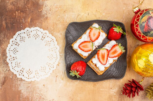 Draufsicht leckere cremige Kuchen mit Früchten und Feiertagsbaumspielzeug auf hellem Hintergrund