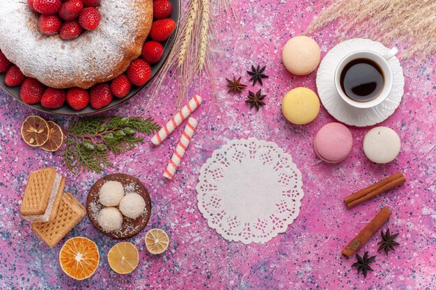 Draufsicht leckere Erdbeerkuchen mit französischen Macarons und Tasse Tee auf rosa