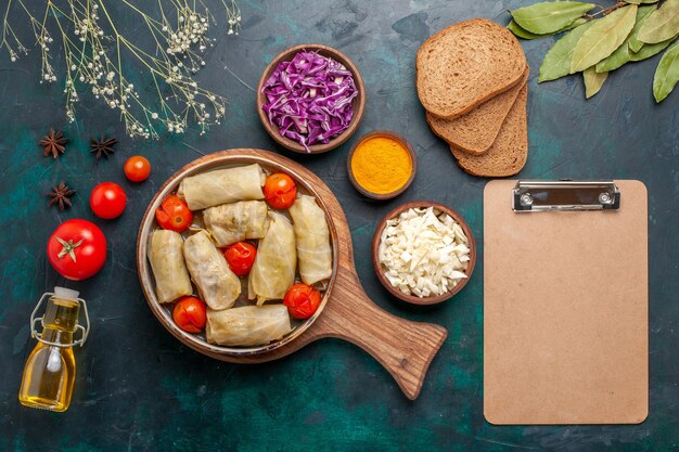 Draufsicht leckere Fleischmahlzeit gerollt mit Kohl und Tomaten genannt Dolma mit Brot und Olivenöl auf dunkelblauem Schreibtisch