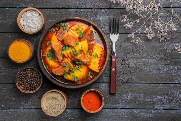 Draufsicht leckere Fleischsuppe mit Kartoffeln und Gewürzen auf dem dunklen Schreibtisch