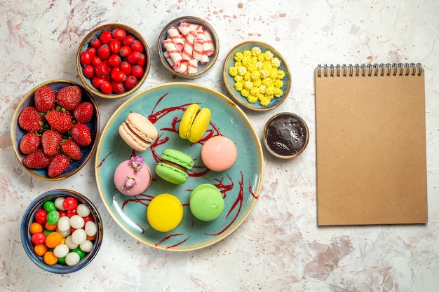 Draufsicht leckere französische macarons mit beeren und süßigkeiten auf weißem schreibtischkuchen süßen keks