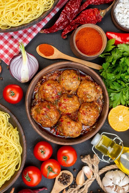 Draufsicht leckere Frikadelle in Schüssel Spaghetti in Schüssel Ölflasche Tomaten Petersilie trockene Paprika auf dem Tisch