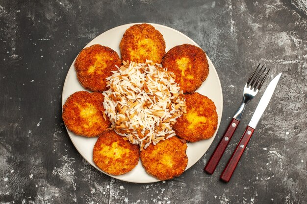 Draufsicht leckere gebratene Schnitzel mit gekochtem Reis auf der dunklen Oberfläche Teller Mahlzeit Foto Fleisch