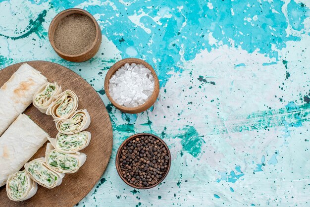 Draufsicht leckere Gemüsebrötchen ganz und in Scheiben geschnitten mit Gemüse und Gewürzen auf dem hellblauen Schreibtisch Essen Mahlzeit Brötchen Gemüse