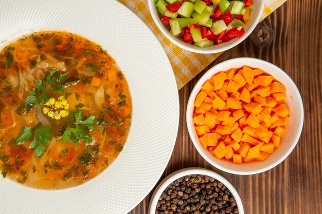 Draufsicht leckere Gemüsesuppe mit Gewürzen auf dem braunen hölzernen Schreibtischsuppenlebensmittelgemüsewürzmehl