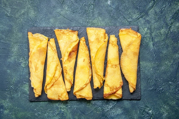 Kostenloses Foto draufsicht leckere gerollte pfannkuchen, die auf dem dunklen hintergrundfarbe-mahlzeitkuchen-fleisch-gebäck-teig-kuchen süßer heißer kuchen gesäumt sind