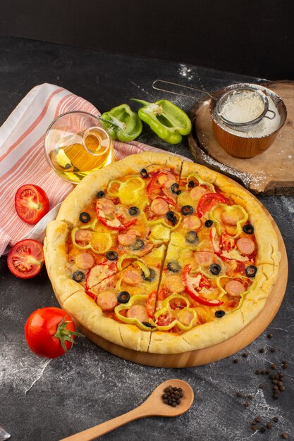 Draufsicht leckere käsige Pizza mit roten Tomaten, schwarzen Oliven und Würstchen auf dem dunklen Schreibtisch mit Öl und frischen Tomaten Fast-Food-Italienischer Teig