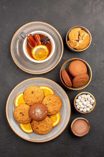 Draufsicht leckere Kekse mit Tasse Tee und Orangen auf dunklem Hintergrund Keksfrucht süßer Kuchen Keks Zitrus