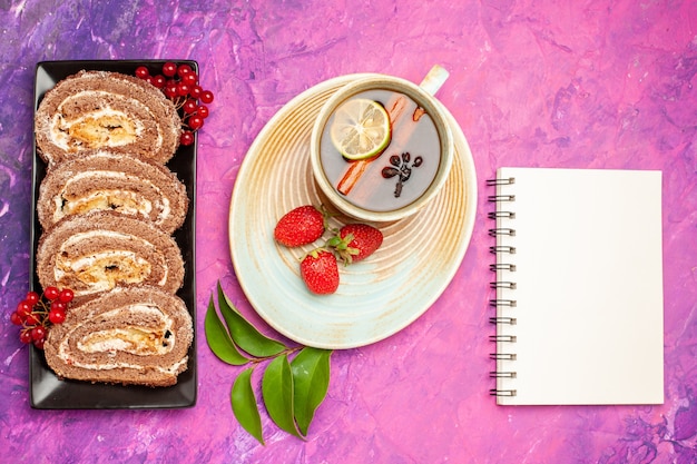 Draufsicht leckere Keksröllchen mit Tasse Tee auf rosa Schreibtisch