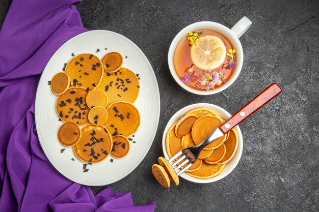 Draufsicht leckere kleine pfannkuchen mit tasse tee auf dunklem hintergrund