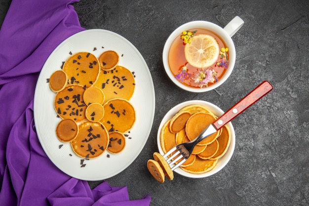 Draufsicht leckere kleine Pfannkuchen mit Tasse Tee auf dunklem Hintergrund