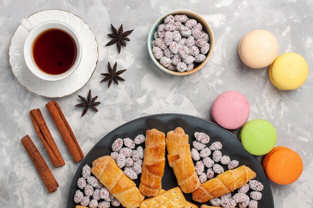 Draufsicht leckere Kuchen mit Bagels Macarons Tasse Tee und Bonbons auf grau-weißer Oberfläche