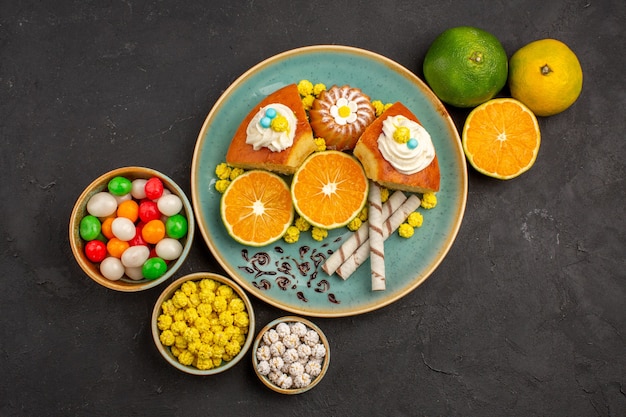 Draufsicht leckere Kuchenstücke mit frisch geschnittenen Mandarinen und Süßigkeiten auf Dunkelheit