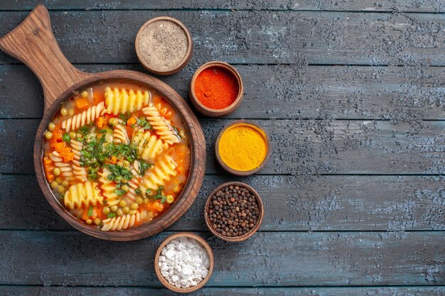 Draufsicht leckere Nudelsuppe aus spiralförmiger italienischer Pasta mit verschiedenen Gewürzen auf der dunklen Schreibtischsuppe Farbe italienisches Nudelgericht