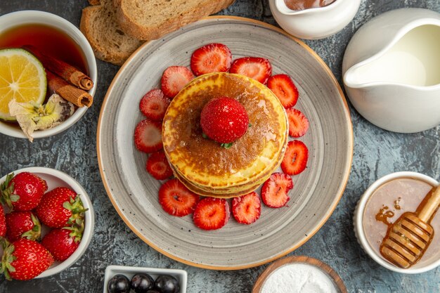 Draufsicht leckere Pfannkuchen mit Tasse Tee und Früchten auf Licht